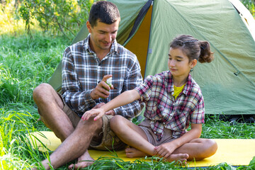 Dad sprays repellent on daughter outdoor camping and picnicking near a tent	

