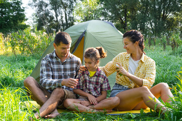 Family uses a reppelent outdoor camping and picnicking near a tent	
