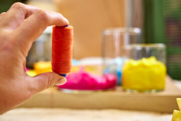 Close-up of a spool of sewing thread in hand against the blurred background of the workshop