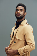 Obraz premium Stylish African man in a beige trench coat poses confidently against a gray background, showcasing modern fashion and self assurance for contemporary lifestyle images