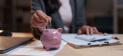 Businesswoman putting coin into piggy bank after calculating tax with calculator, managing...