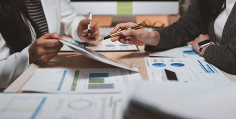 Businesswomen are discussing financial charts and statistics during a meeting, collaborating on...