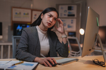 Young business professional experiencing a headache while working on her computer in a dimly lit...