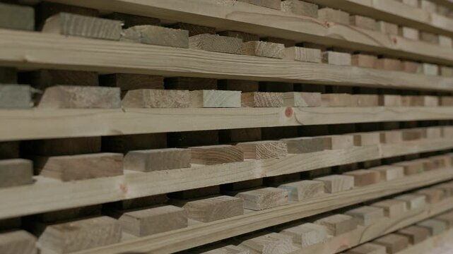 Rows of timber planks neatly stacked with drying spacers in between, allowing airflow for proper seasoning, captured in a lumber facility with warm, natural textures