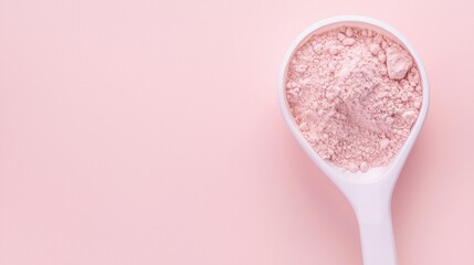 A scoop of pink powder rests on a soft pink background, emphasizing texture and color in a minimalist presentation.