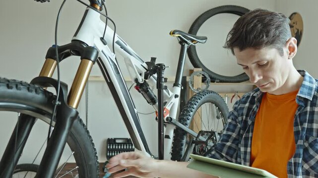 A male bicycle mechanic in the repair shop disassembles a mountain bike and repairs it. Maintenance concept, preparation for the new season