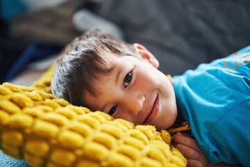 Smiling boy lying on yellow pillow in cozy home environment