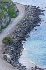 A dirt road carved out on the shoreline of a rocky bluff winds between sea and land. and is...