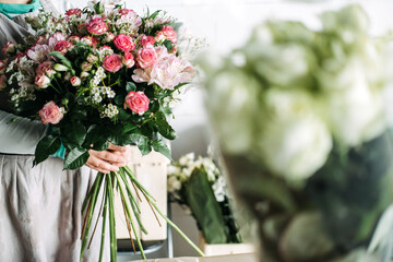 Florist holding a completed bouquet of pink roses, alstroemeria, and baby's breath in studio....