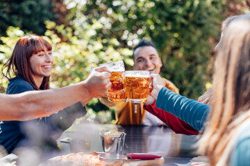 Friends toasting with beer mugs at outdoor party in a sunny day