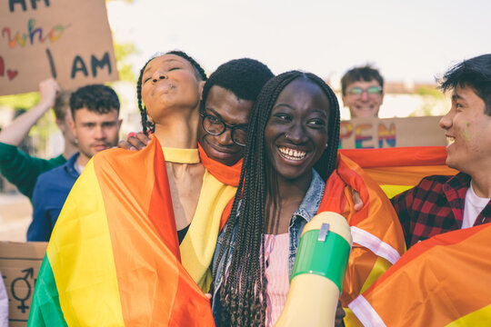 Happy multiethnic activists embracing with a rainbow flag at lgbtq pride parade