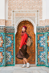 Young woman with backpack walking at the door to the Ben Youssef Medersa Quranic school in Marrakech, Morocco, enjoying her trip