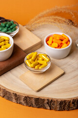 Many colored vitamin pills in small bowls from above on wooden desk on orange background. Rustic composition with food supplements. Dietary supplements and healthy lifestyle. Vitamins and minerals.