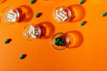 Dietary supplements, vitamins and minerals pills in small plates from above on an orange background.
