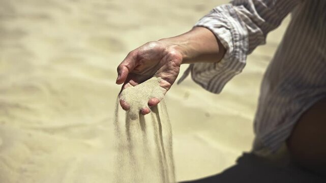 Female hand against sand background with quartz silicon oxide slowly sifting through fingers. Showcases this versatile material used in construction and microchips.