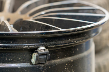 Close-up of alloy wheel rim with tire pressure monitoring sensor (TPMS) installed. Detailed macro view of dirty automotive wheel showing modern safety technology sensor mounted on premium silver rim