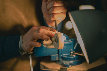 Focused on the violin scroll, this Cremona craftsman uses a chisel and a bright lamp, highlighting the fine details of carving with tradition-rich tools on a classic wooden workbench setting.
