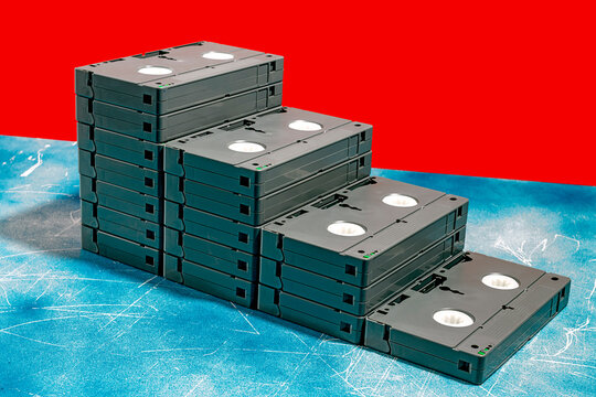 Stack of VHS tapes arranged like a staircase on a blue surface with a red background