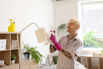 Young tattooed man cleaning lamp at home