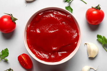 Bowl with tomato paste and fresh vegetables on grey background