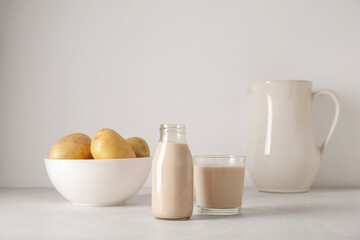 Bottle and glass of tasty potato milk on light background