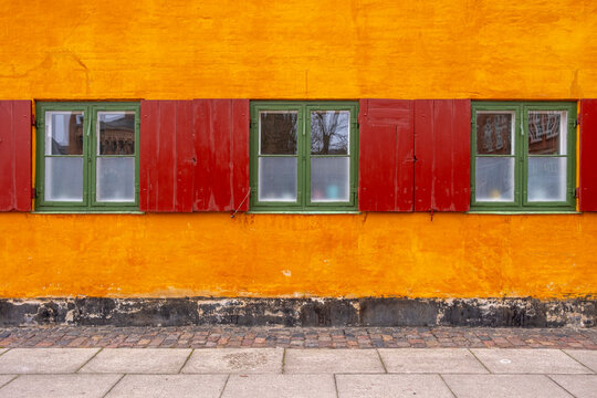 Symmetrical wall in Nyboder, Copenhagen, with rhythmic window placement and rich yellow and red hues under diffused natural light.