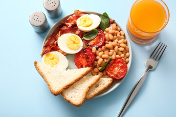 Plate with tasty English breakfast and glass of juice on blue background