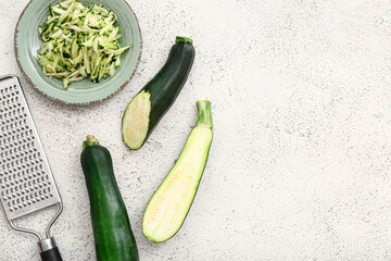 Bowl with slices of fresh green zucchini and grater on white background