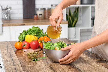 Woman adding olive oil into bowl with tasty salad at table in kitchen