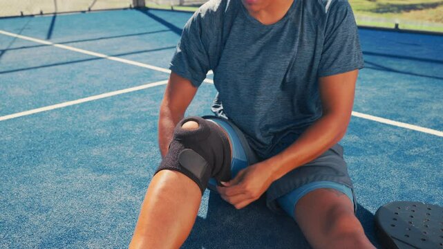 Sport athlete, injury and hands with knee brace on court for pain management, joint support or fitness accident. Padel tennis, person and kneecap protection for tournament practice or sprain recovery