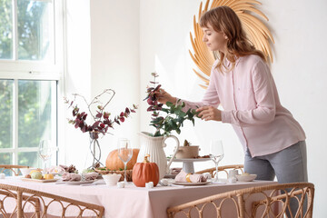 Beautiful young woman decorating table for Thanksgiving Day dinner in dining room