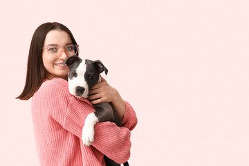 Beautiful young woman in eyeglasses with cute staffordshire terrier puppy on pink background