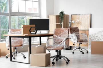 Interior of modern office with chairs wrapped in stretch film and cardboard boxes on moving day