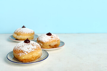 Plates with tasty donuts for Hanukkah celebration on light table against color background