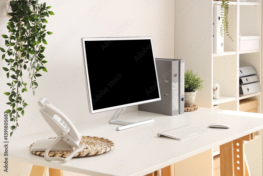 Poster blank computer monitor with telephone on table in light office