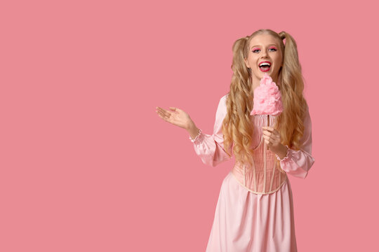 Beautiful young happy woman dressed as doll with cotton candy on pink background