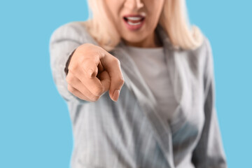 Mature woman pointing at viewer on blue background, closeup. Accusation concept