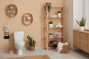 Interior of stylish bathroom with houseplants and ceramic toilet bowl near beige wall