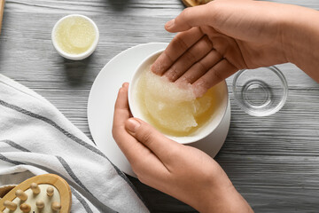 Female hands with bowl of body scrub on grey wooden background, closeup