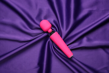 Pink vibrator from sex shop on purple fabric background