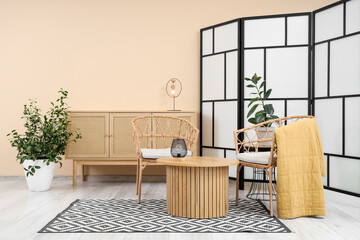 Interior of stylish living room with folding screen, drawers and armchairs