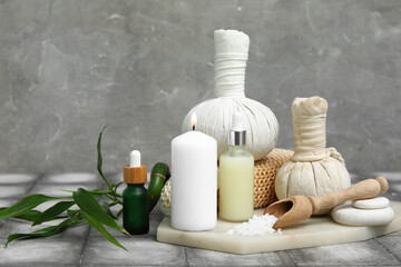 Bottles of cosmetic oil with herbal bags, sea salt, spa stones and burning candle on grey tile table
