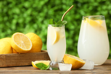 Glass and jug of fresh lemonade with mint on wooden table outdoors