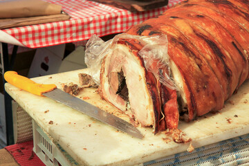 Close-up of Italian porchetta, a traditional pork roll, lying on a cutting board with a knife.