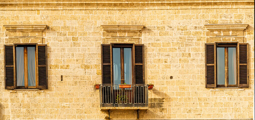 old yellow facade of house with three brown vintage wooden windows in retro italian european style