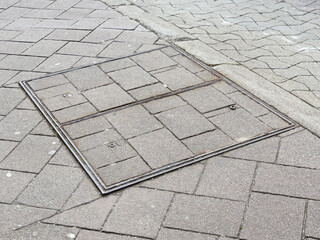 Rectangular metal manhole cover on brick pavement and asphalt road
