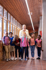 Female teacher with diverse group of school children standing in hallway, smiling together
