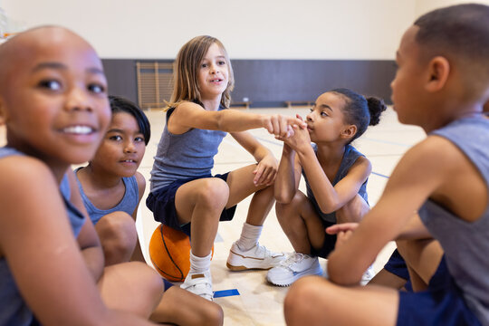 Fototapeta In school gym, diverse children sitting on basketball, talking and bonding as team