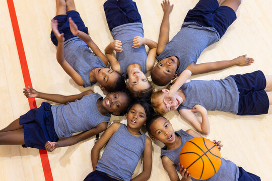 Fototapeta Lying on gym floor, group of school diverse children smiling with basketball