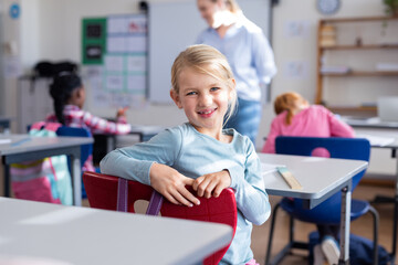 In school, smiling girl sitting at desk in classroom with classmates